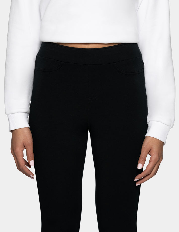 Black high-waisted leggings with side pockets, shown on a model wearing a white cropped sweatshirt against a light gray background.