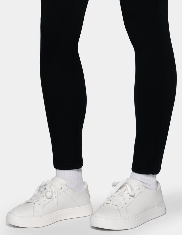 White low-top sneakers worn with white socks and black leggings, shown from the feet up against a light gray background.