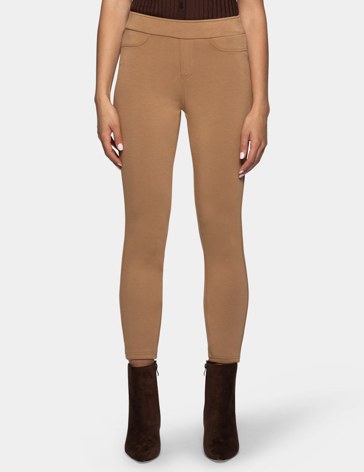 A model wearing slim-fit, ankle-length tan leggings and dark brown ankle boots, set against a light gray background.