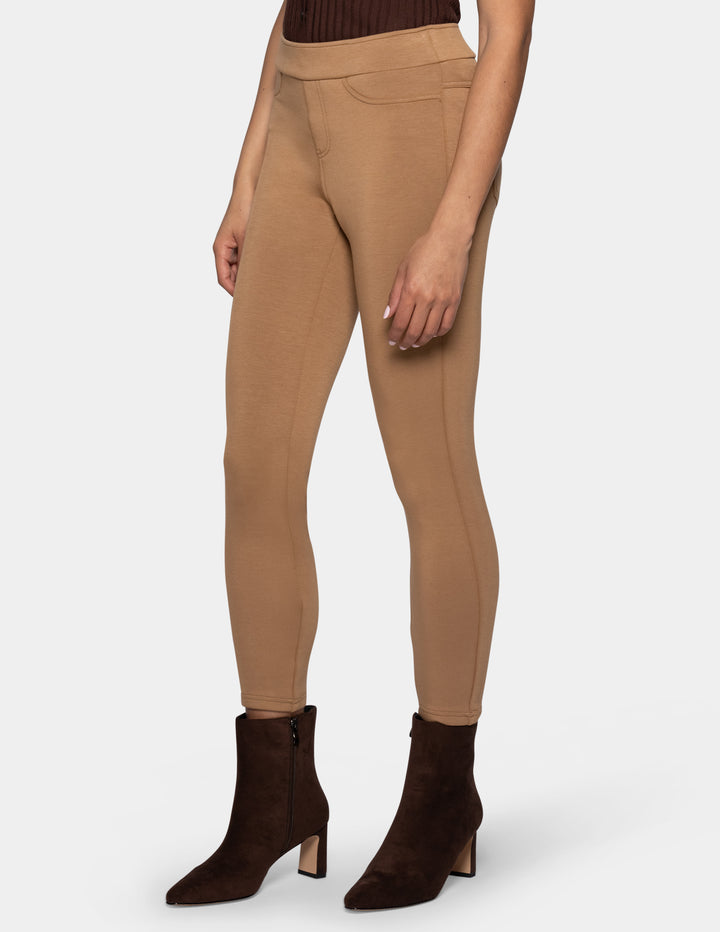 A model wearing slim-fit tan leggings and dark brown heeled ankle boots, shown from the waist down against a light gray background.