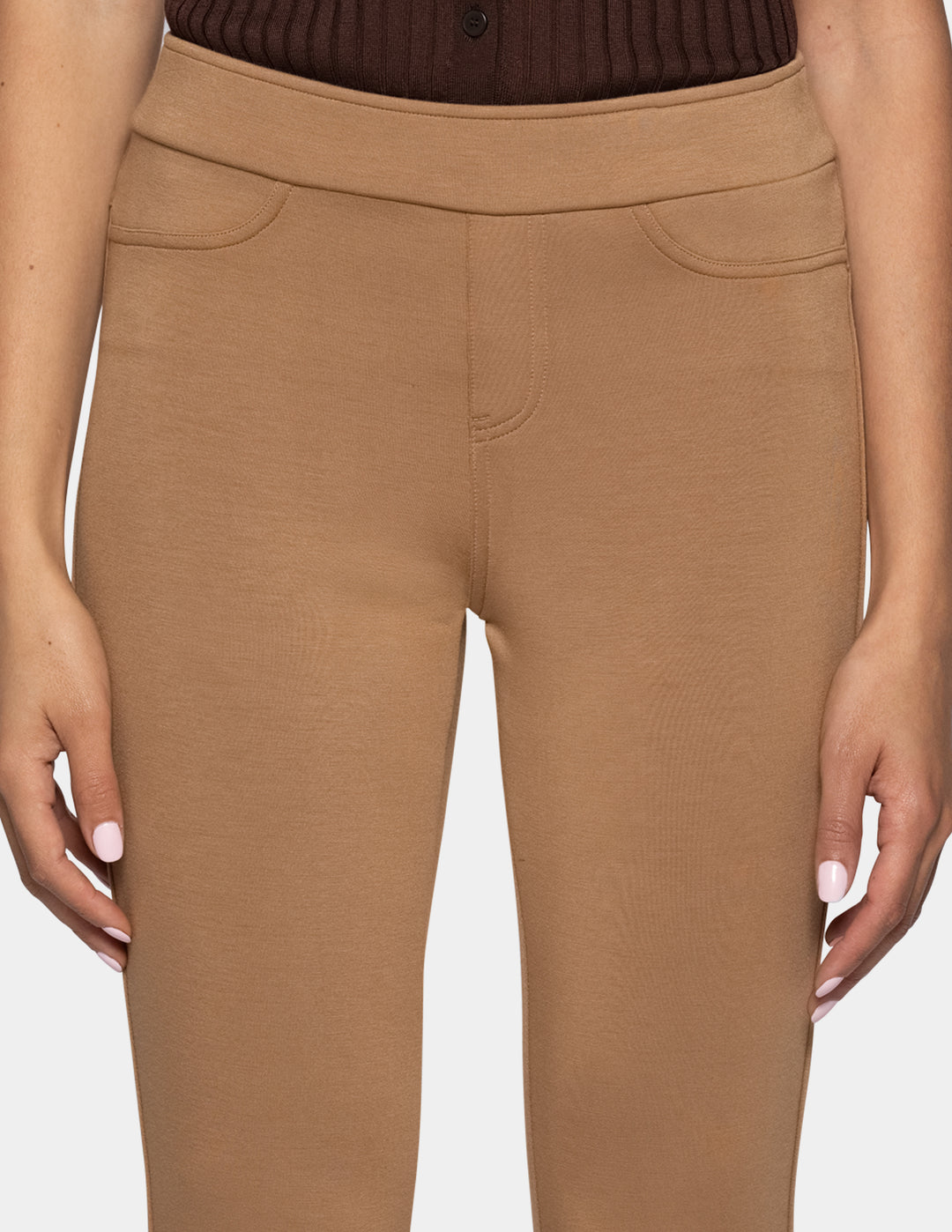 A close-up of a model wearing high-waisted, solid tan leggings with a wide waistband, paired with a dark brown ribbed top.