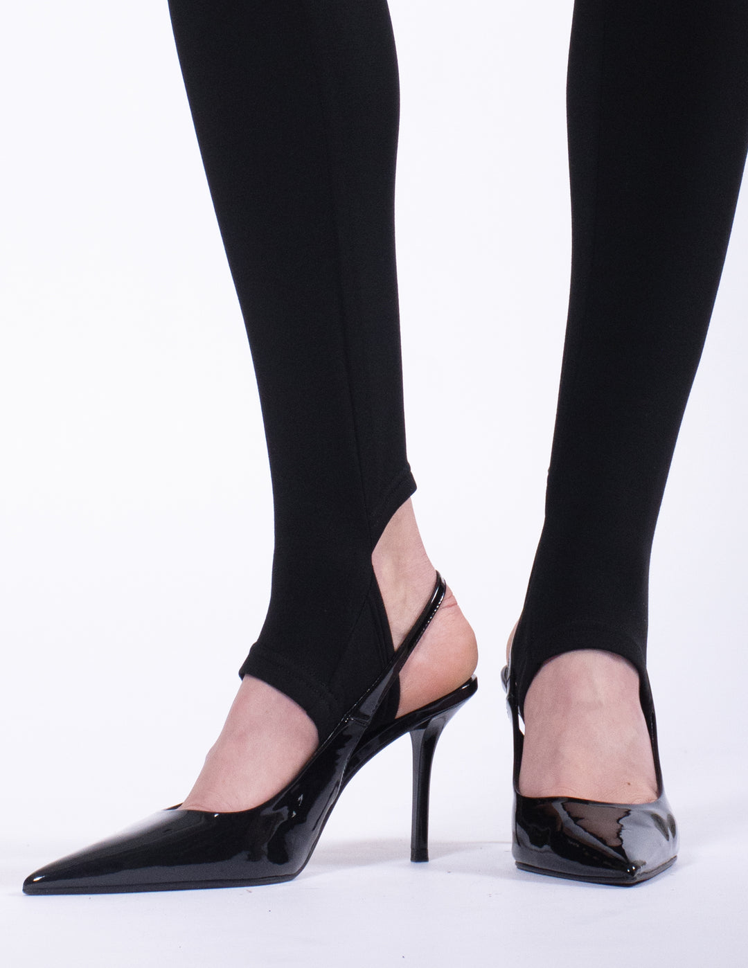 Black high-heeled shoes worn with black leggings on a white background