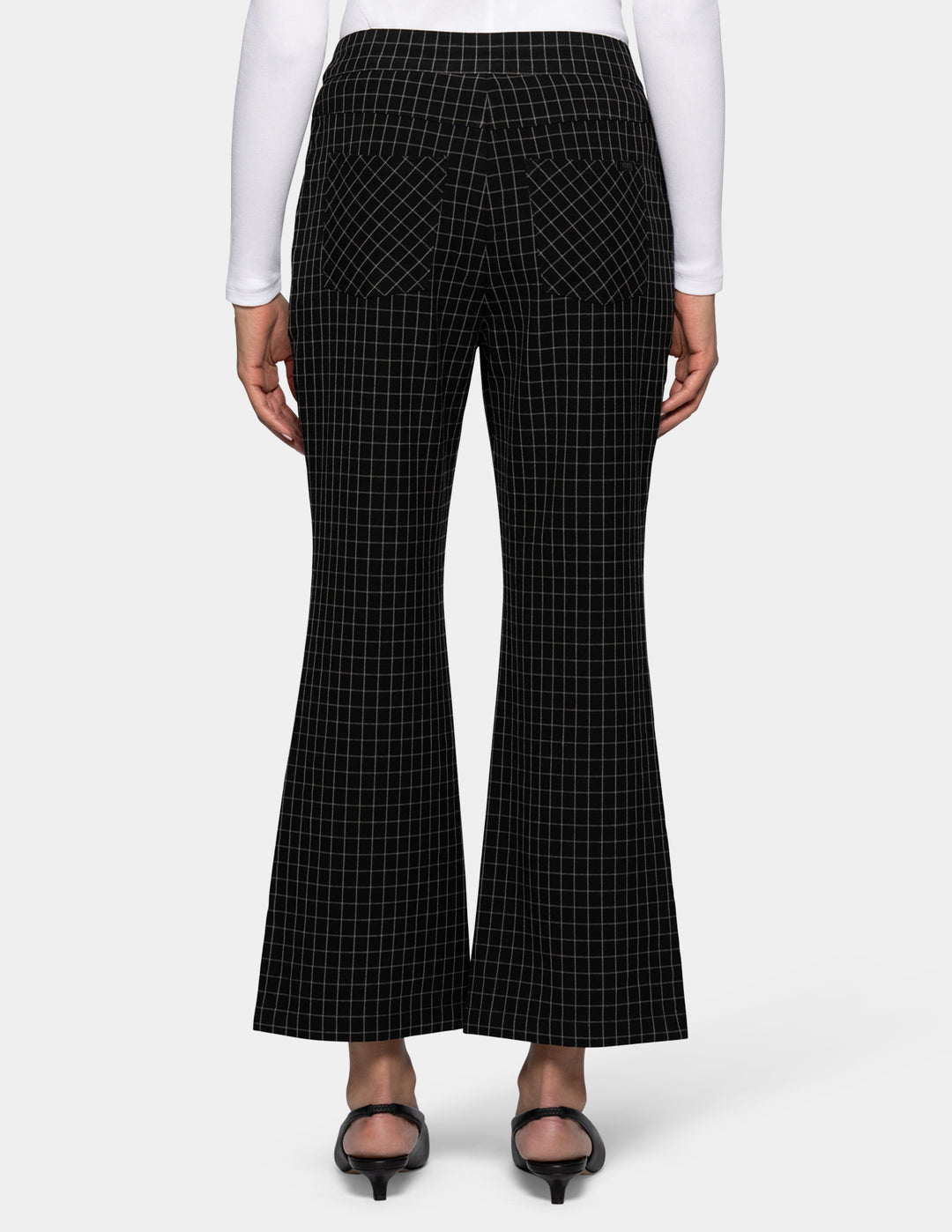 Black flare cropped pants with a white windowpane grid pattern, shown on a model from the backside wearing a white long-sleeve top and black kitten heels against a light gray background.