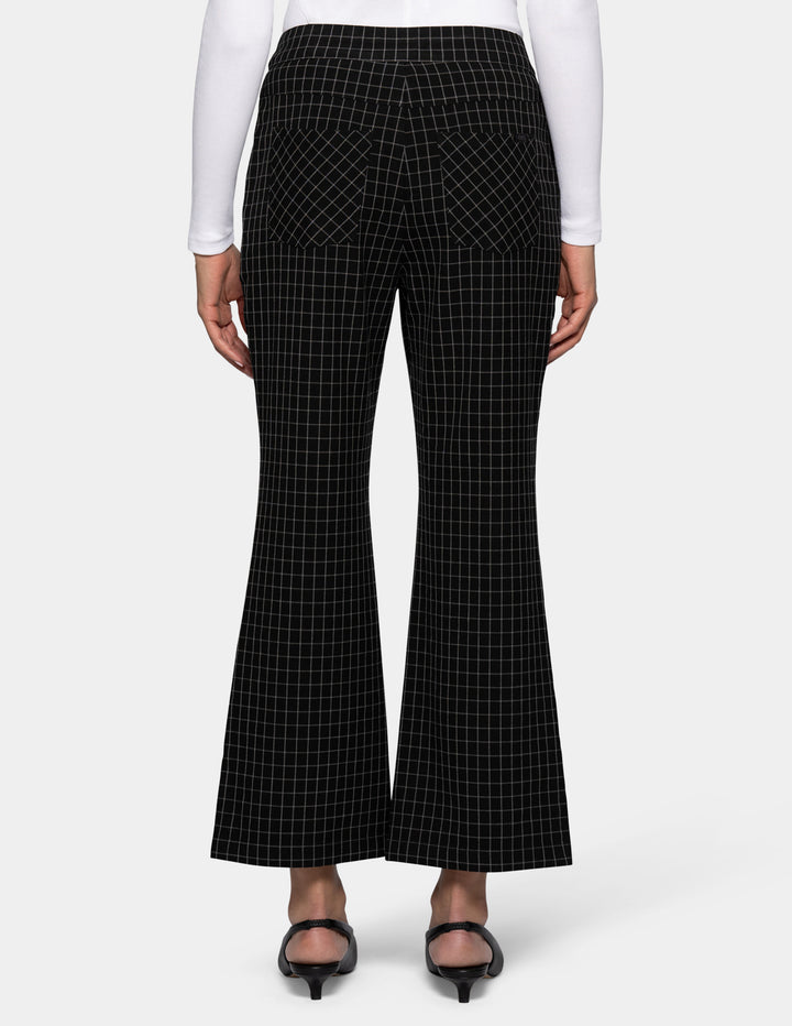 Black flare cropped pants with a white windowpane grid pattern, shown on a model from the backside wearing a white long-sleeve top and black kitten heels against a light gray background.