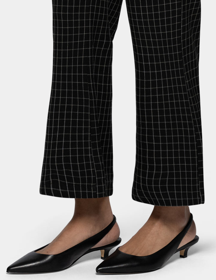 Black pointed-toe slingback kitten heel pumps worn with black flare pants featuring a white windowpane grid pattern, shown on a model's feet against a light gray background.