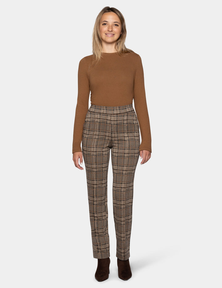 A model wearing brown plaid pants styled with a dark tan long sleeve top, and suede brown boots, against a plain gray studio background.