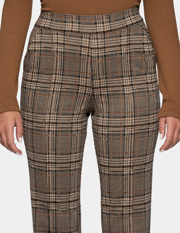 A close-up of a model wearing brown plaid pants styled with a dark tan long sleeve top, against a plain gray studio background.