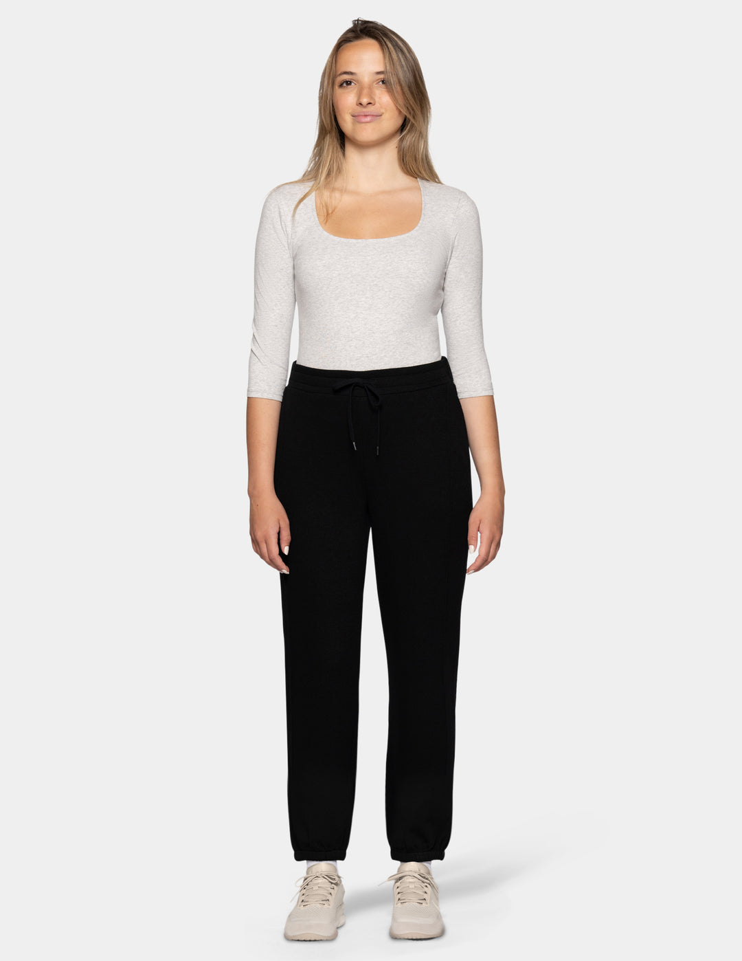 A woman modeling a light heather gray scoop-neck long-sleeve top and black sweatpants against a light gray studio background.