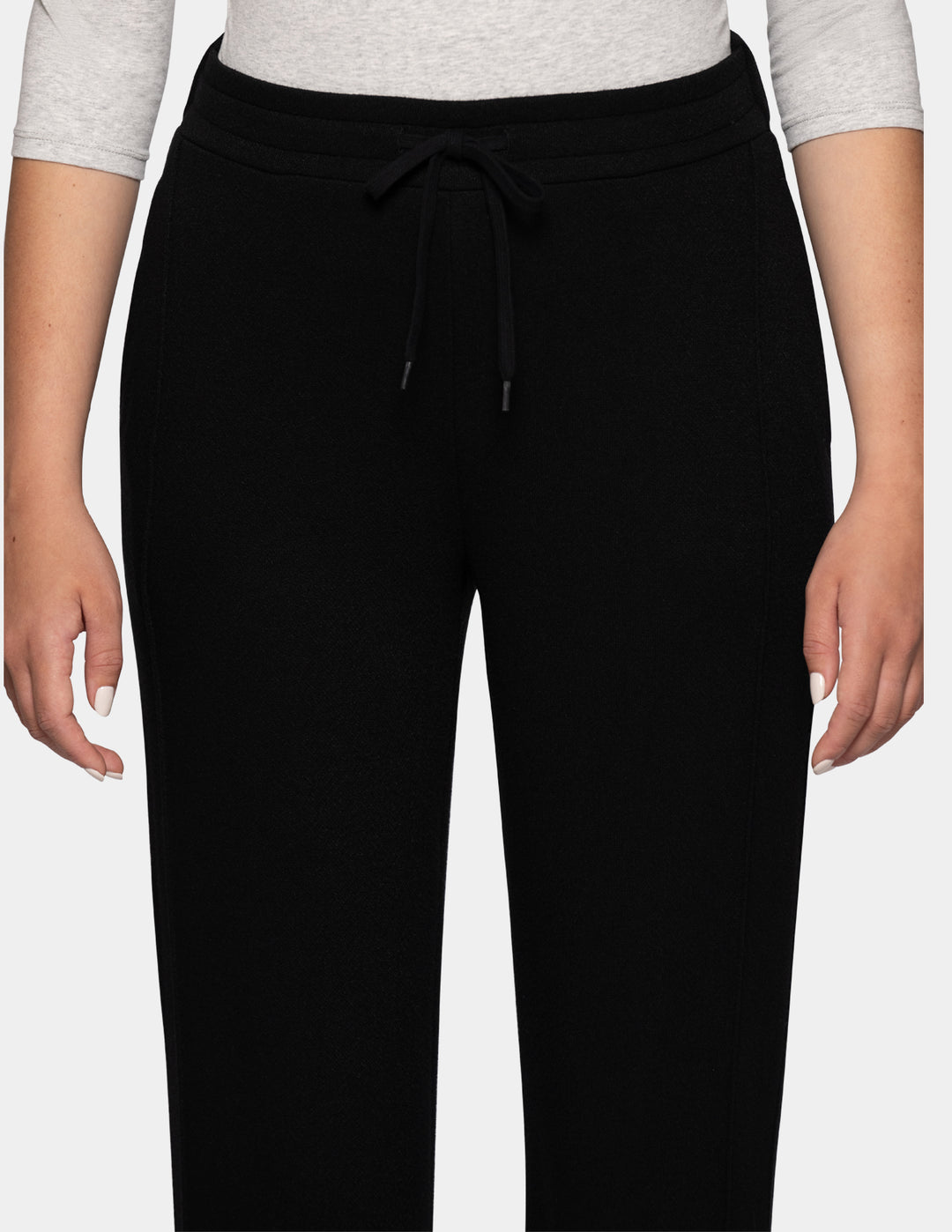 A close-up of a model wearing black jersey trackpants against a gray background.