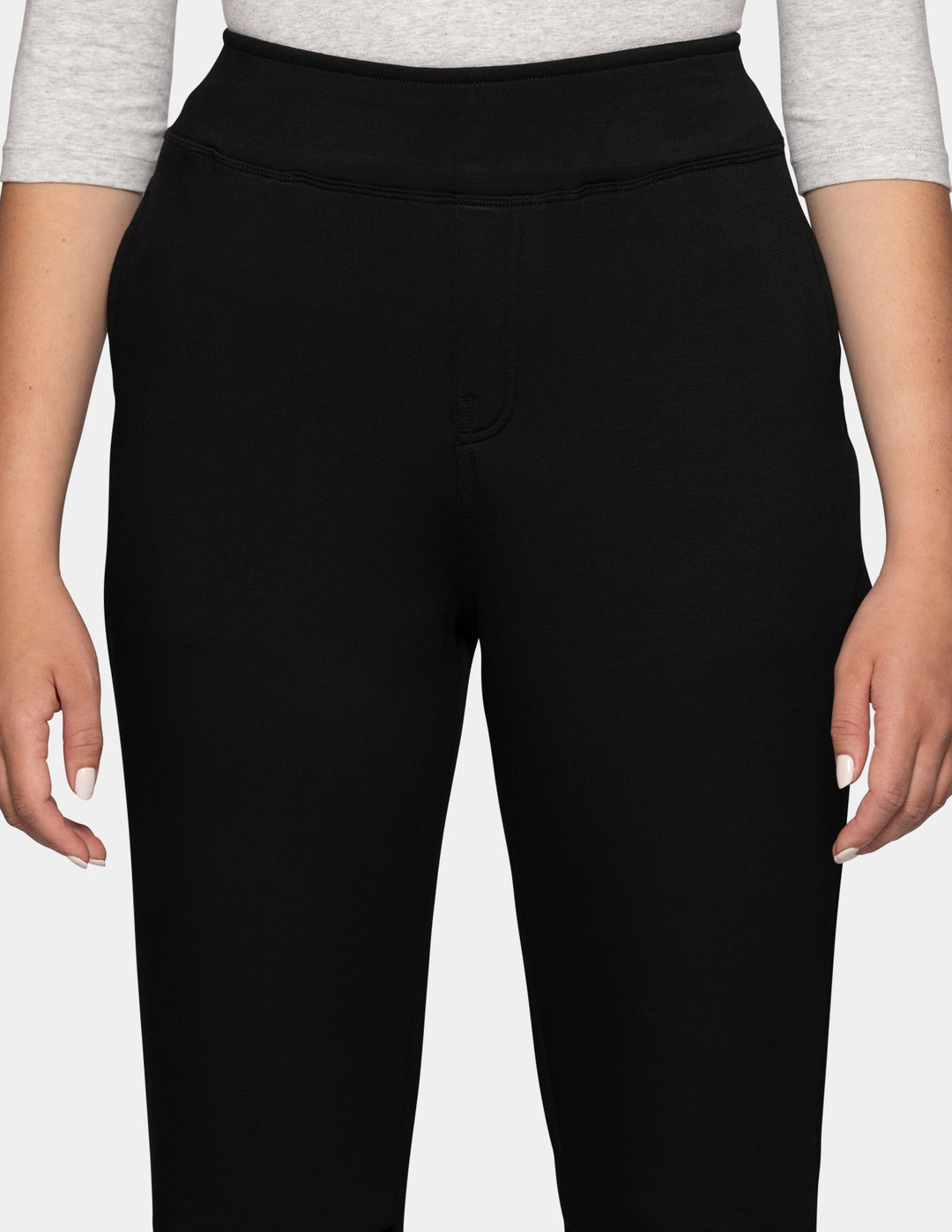 A close-up of a model wearing black hi-rise joggers against a gray background.
