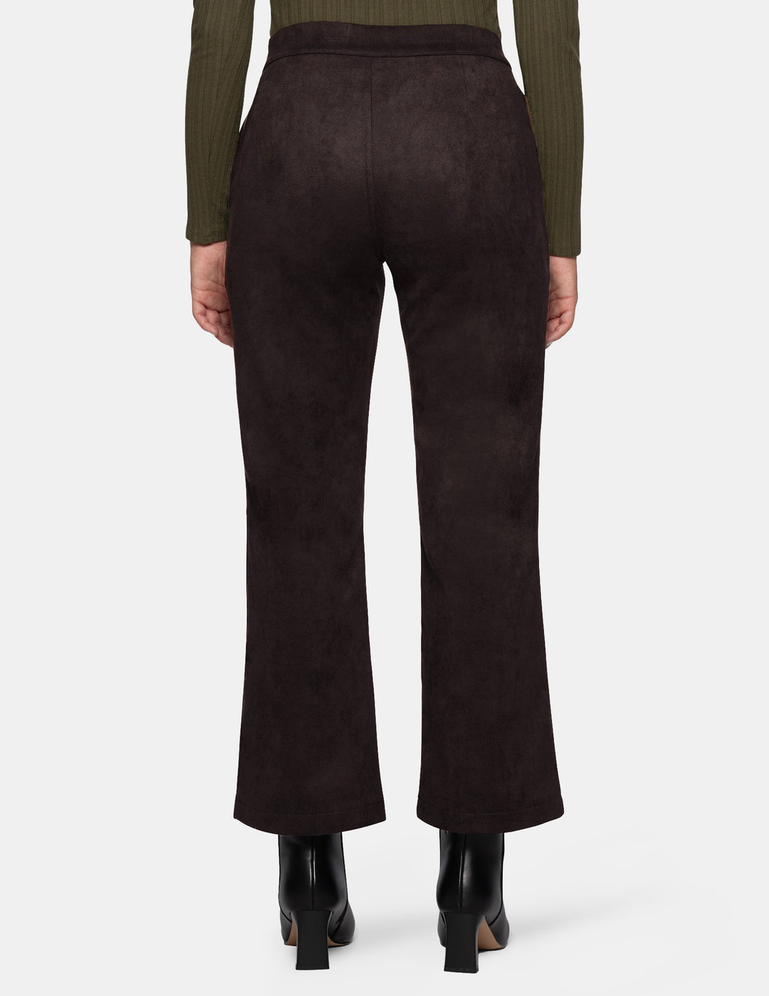 The back view of a model wearing dark brown suede flare pants paired with a long sleeve olive top and black boots, photographed against a light grey background.
