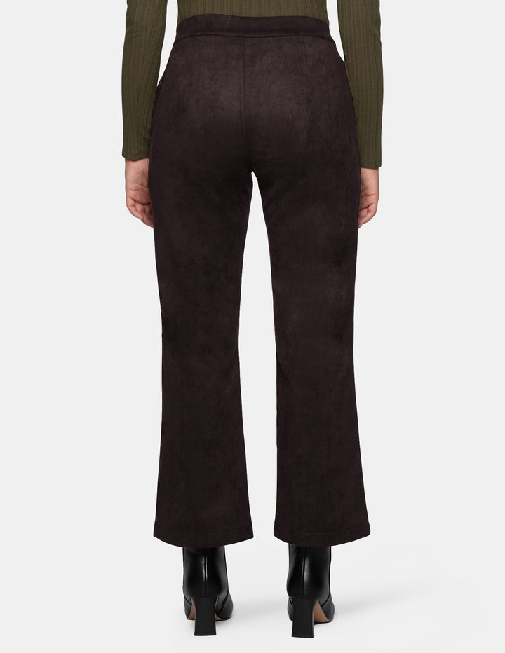 The back view of a model wearing dark brown suede flare pants paired with a long sleeve olive top and black boots, photographed against a light grey background.