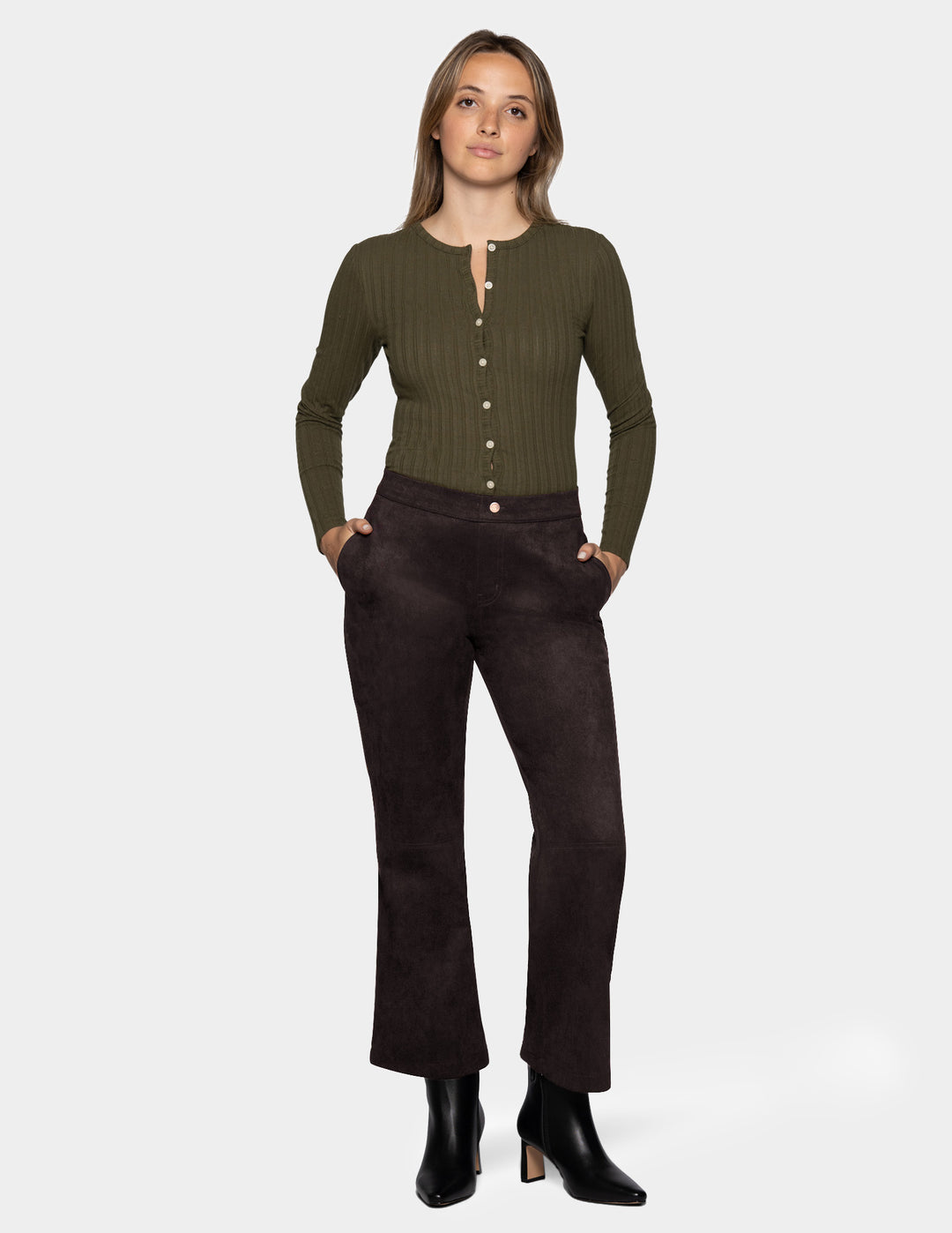 A model wearing dark brown suede flare pants paired with a long sleeve olive top and black boots, photographed against a light grey background.