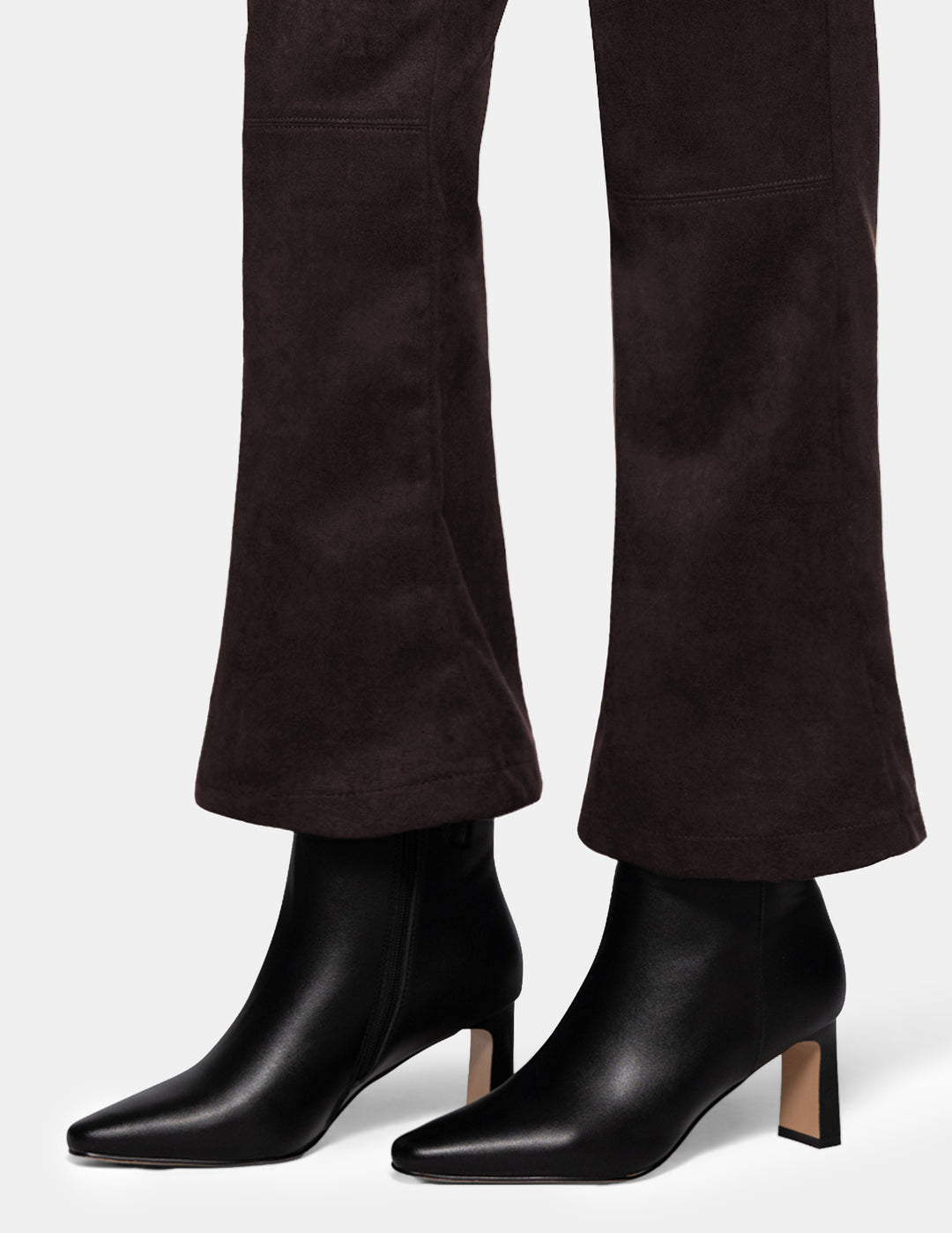 A model wearing dark brown suede flare pants paired with black boots, photographed against a light grey background.
