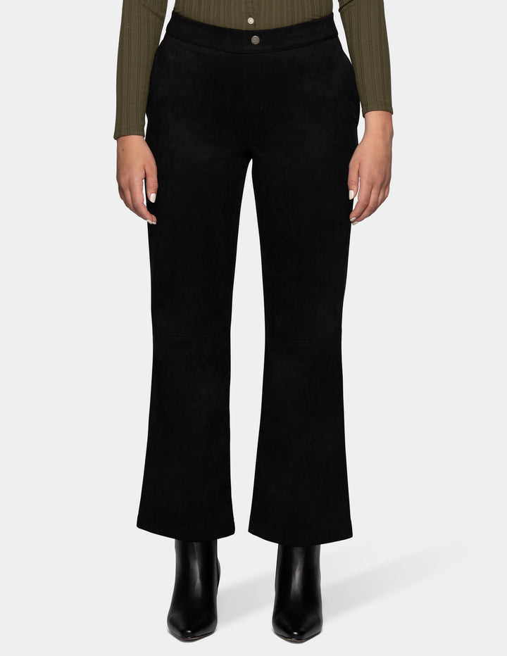 A model wearing black flare pants, an olive green long sleeve top, and black booties, photographed against a light grey background.