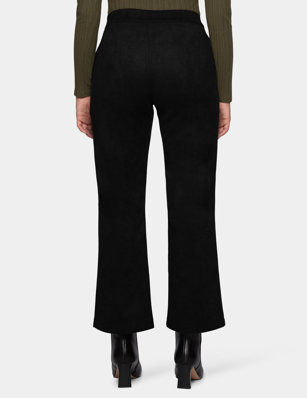 A backside view of a model wearing black flare pants, an olive green long sleeve top, and black booties, photographed against a light grey background.