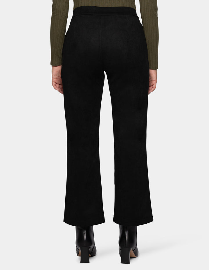 A backside view of a model wearing black flare pants, an olive green long sleeve top, and black booties, photographed against a light grey background.
