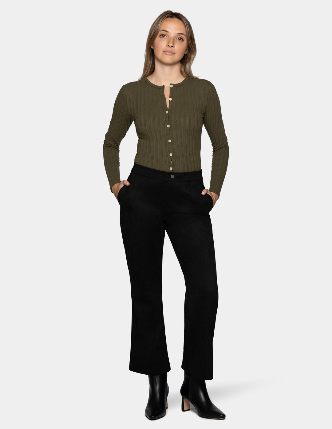 A model wearing black flare pants, an olive green long sleeve top, and black booties, photographed against a light grey background.