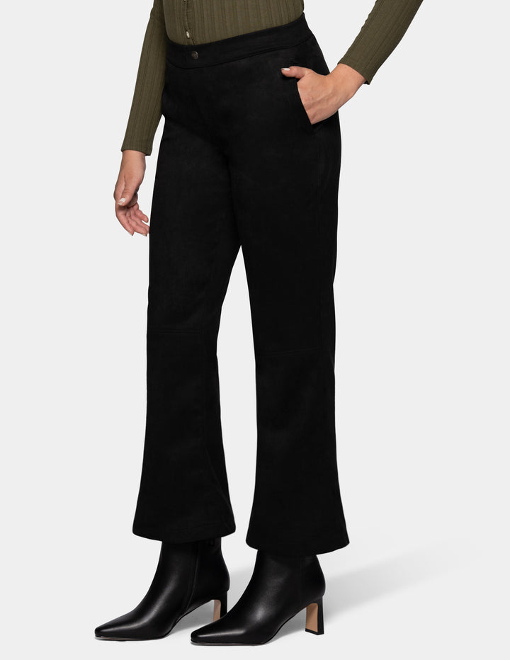 A sideview of a model wearing black flare pants, an olive green long sleeve top, and black booties, photographed against a light grey background.