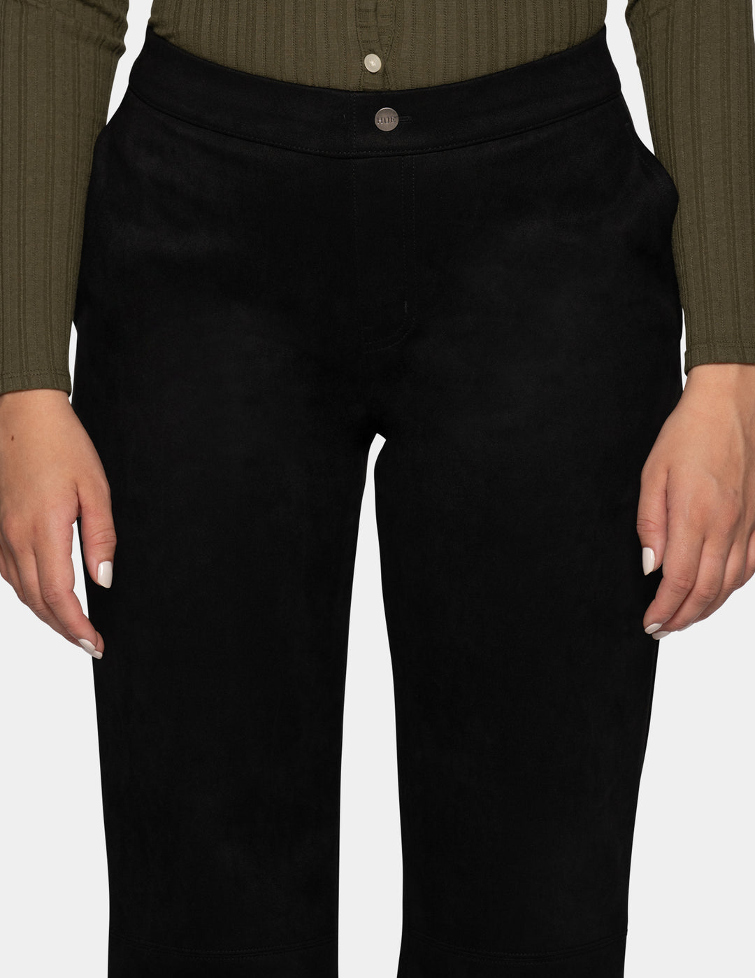 A close-up of a model wearing black pants, and an olive green long sleeve top photographed against a light grey background.