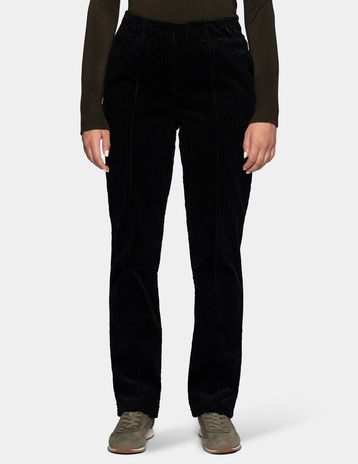 A model wearing black corduroy pants with an olive green long sleeve top and sneakers.