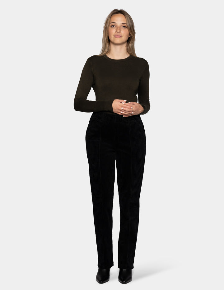 A model wearing black corduroy pants, an olive green long sleeve top, and black boots.