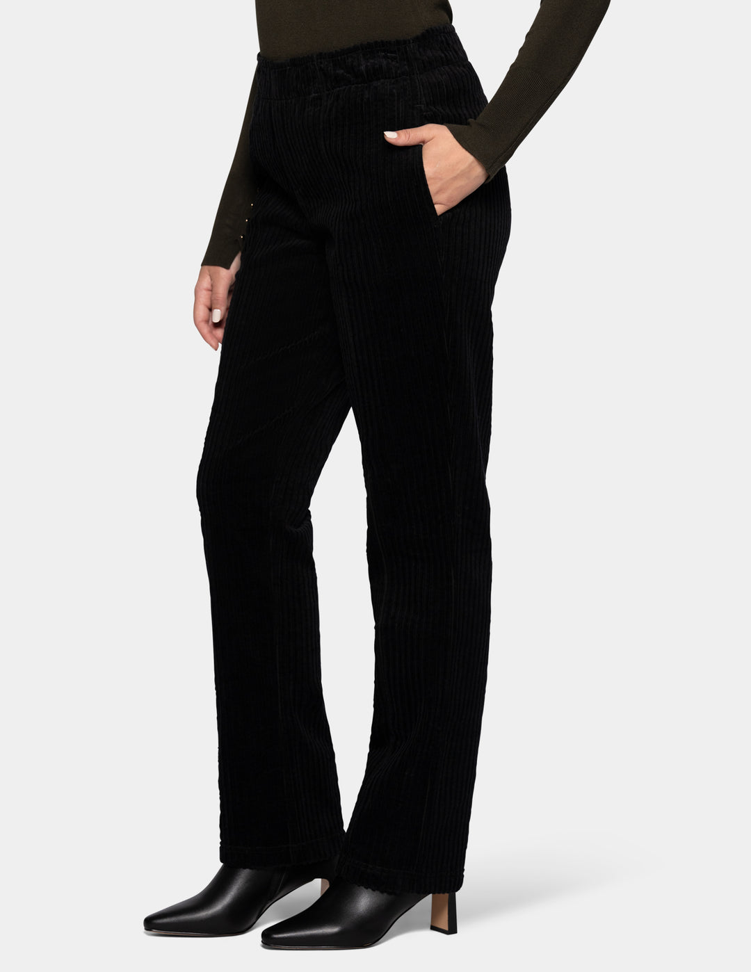 A model wearing black corduroy pants, an olive green long sleeve top, and black boots.