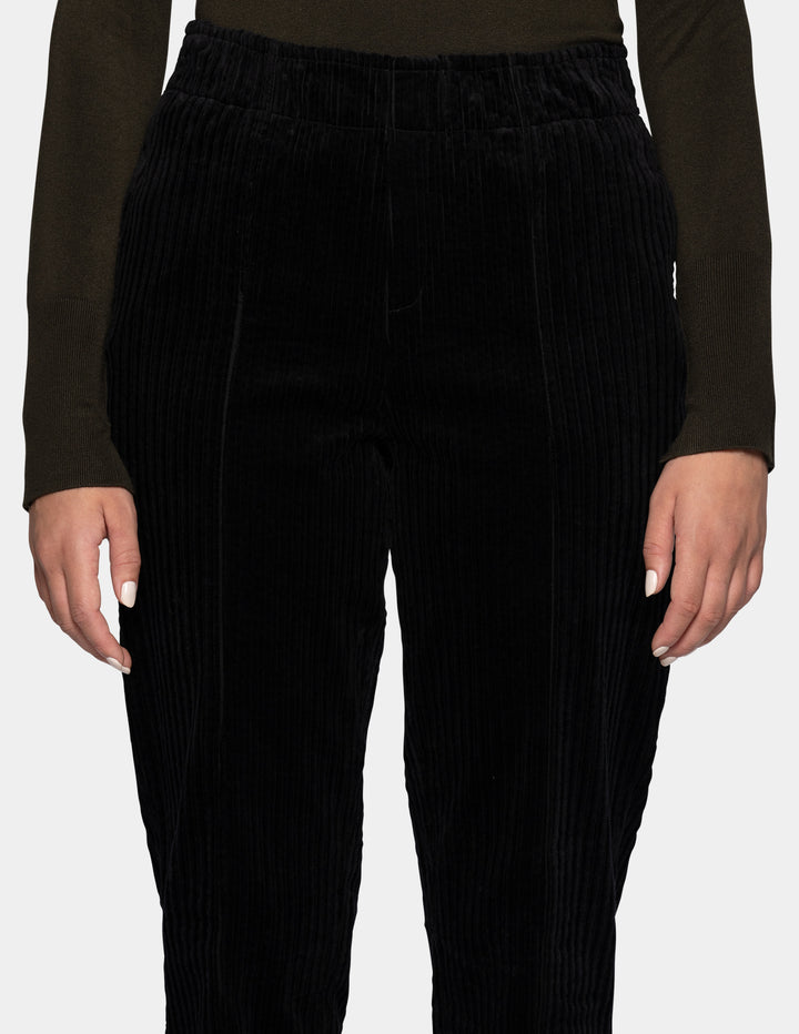 A model wearing black corduroy pants, and an olive green long sleeve top.