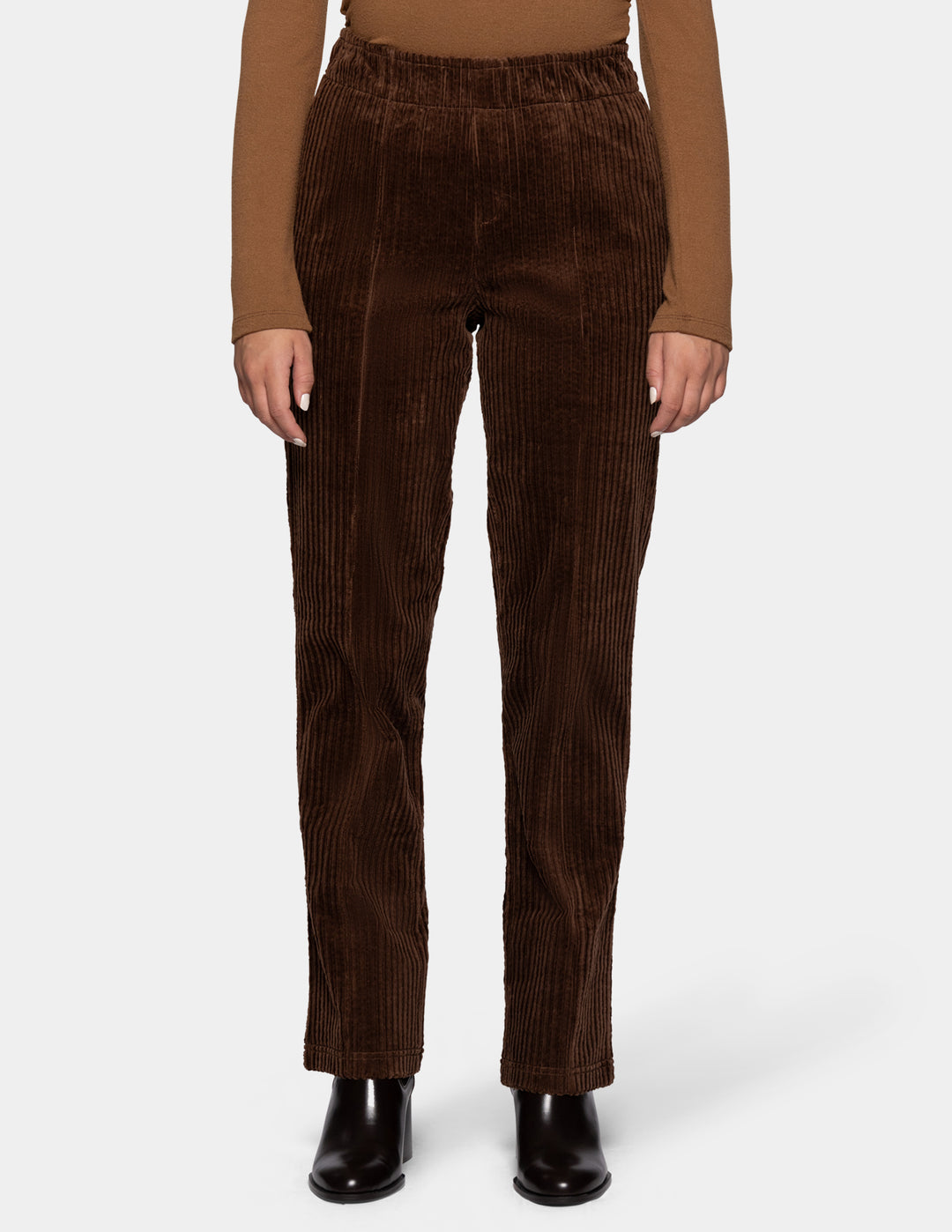 A model wearing brown straight leg corduroy pants paired with a lighter brown long sleeve top and black boots, photographed against a light gray background.