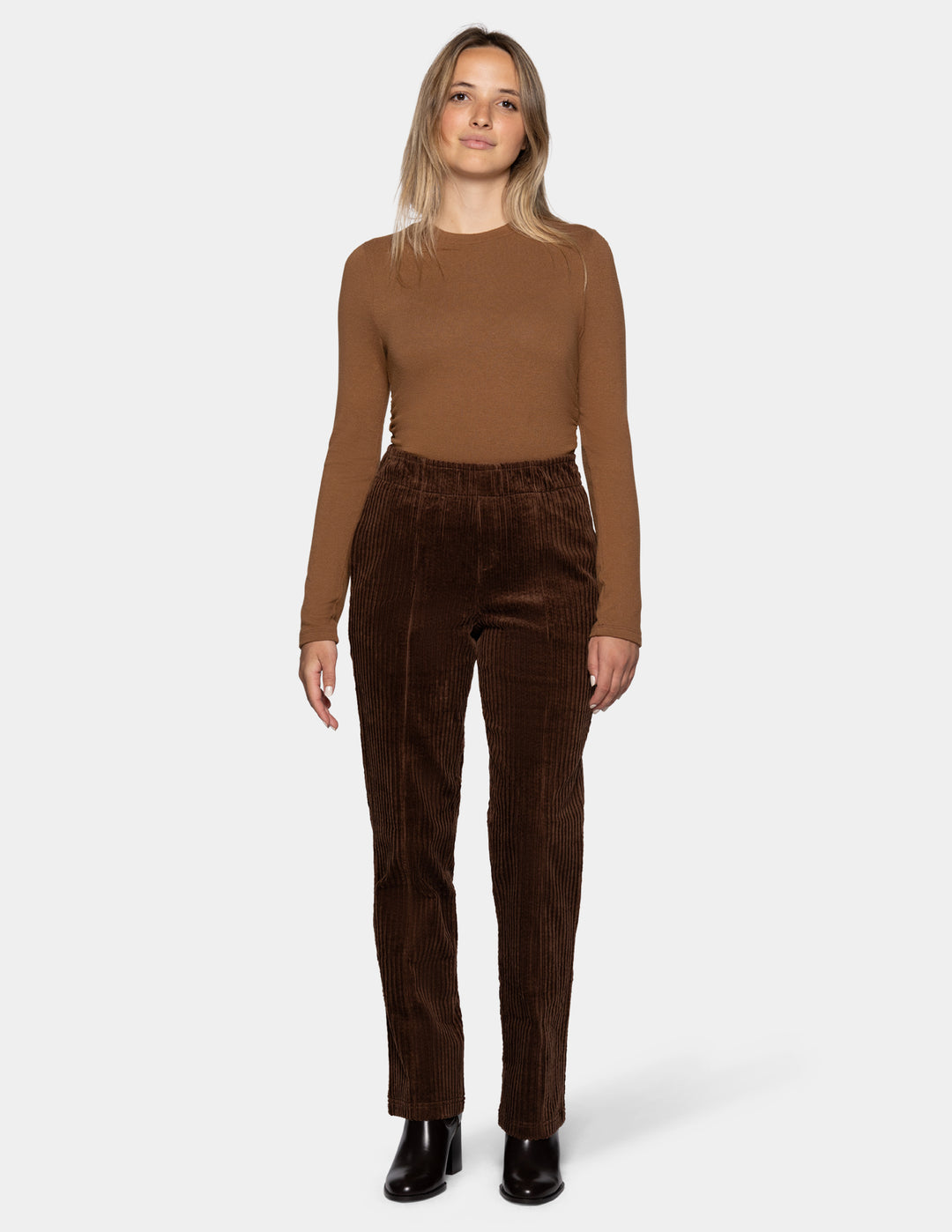 A model wearing brown straight leg corduroy pants paired with a lighter brown long sleeve top and black boots, photographed against a light gray background.