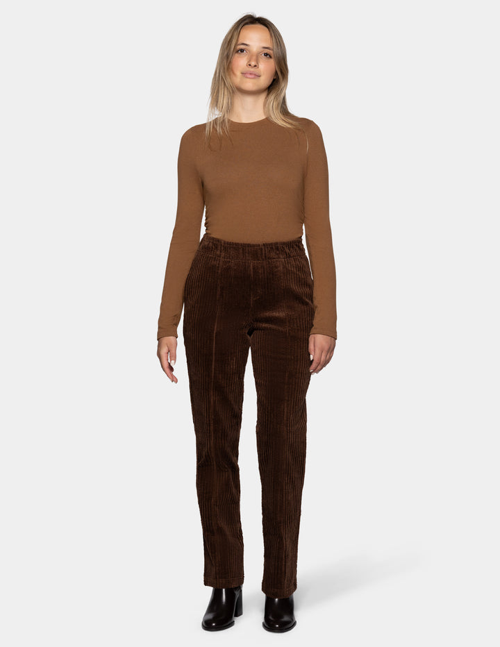 A model wearing brown straight leg corduroy pants paired with a lighter brown long sleeve top and black boots, photographed against a light gray background.