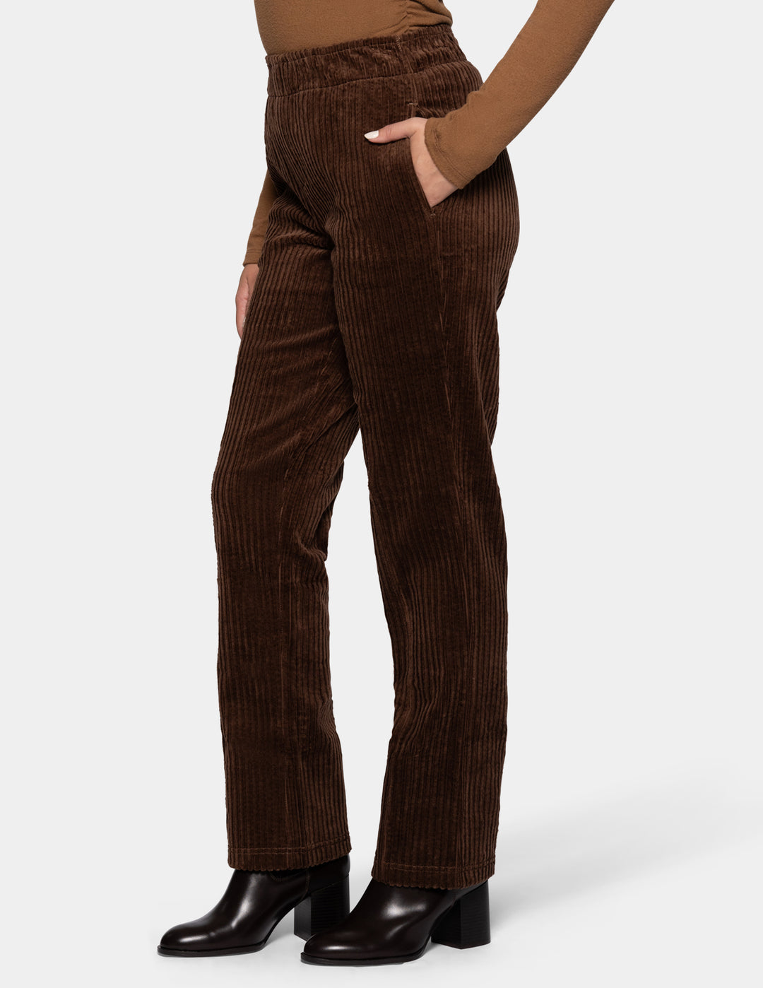 A sideview of a model wearing brown straight leg corduroy pants paired with a lighter brown long sleeve top and black boots, photographed against a light gray background.
