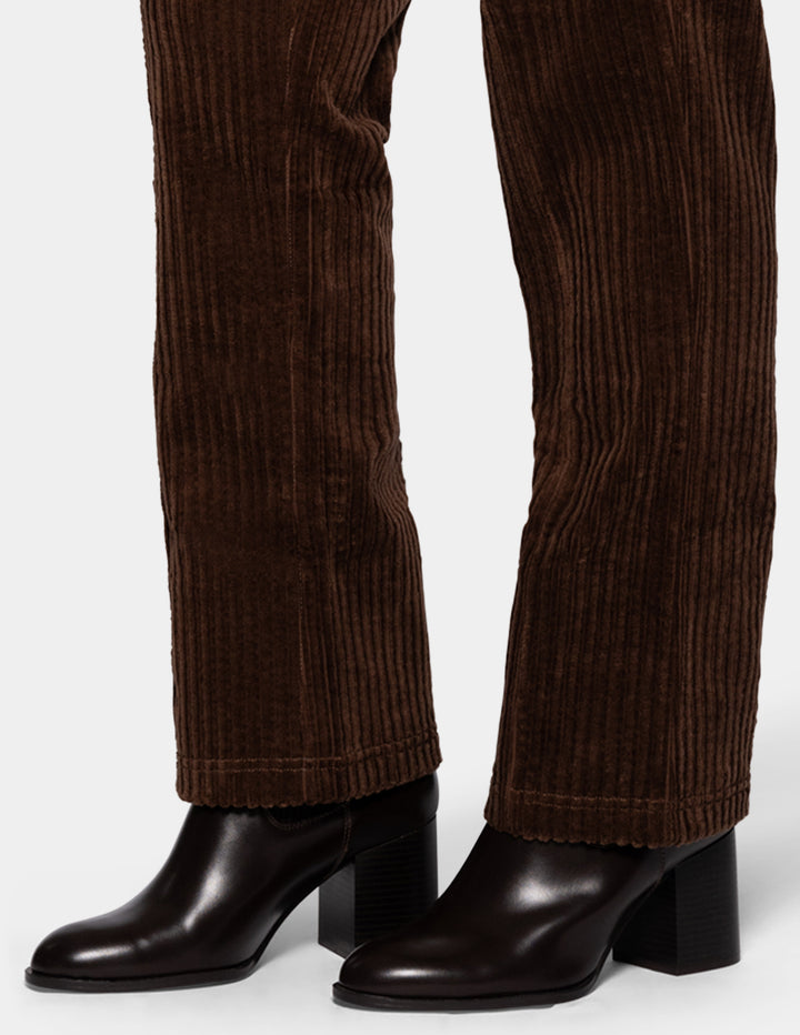 A detailed view of a model wearing brown straight leg corduroy pants paired with black boots, photographed against a light gray background.