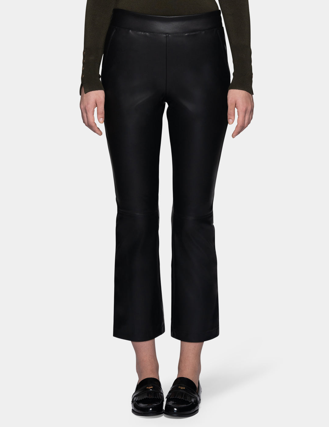 A model wearing black faux-leather cropped pants with a subtle sheen, styled with a dark olive green long-sleeve top and black loafers against a light gray studio background.