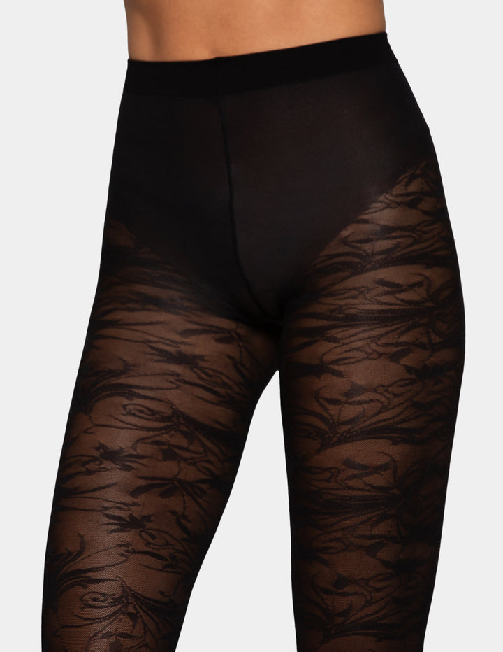 Black sheer brocade tights with a floral pattern shown on a model's legs against a light gray background.