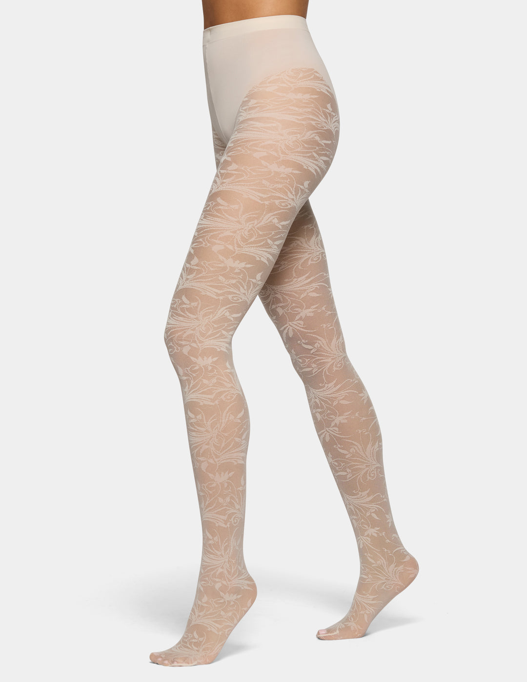 A model's legs wearing sheer nude tights with a delicate white floral pattern, shown against a light gray studio background.