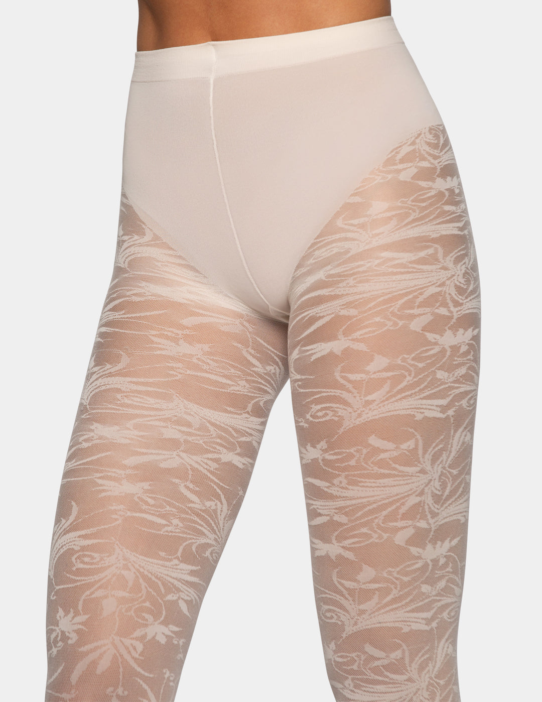 A close-up of a model's legs wearing sheer floral lace tights in a light beige color over nude skin, paired with a matching beige waistband.