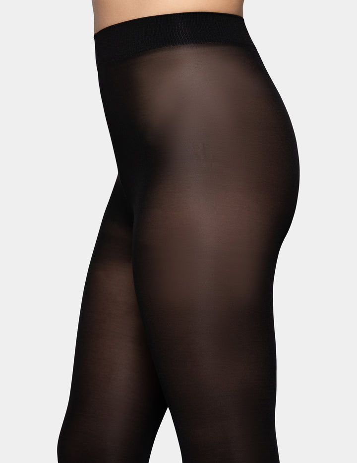 Black tights worn on a model shown from the waist down against a light gray background.