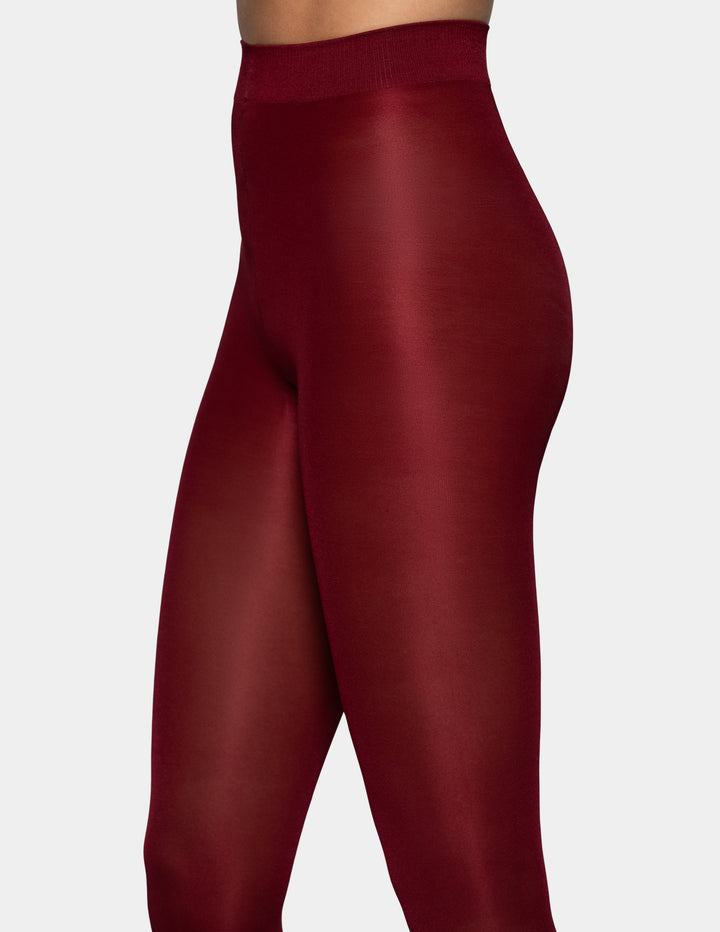 A close-up view of a model's legs wearing dark red tights against a light gray background.