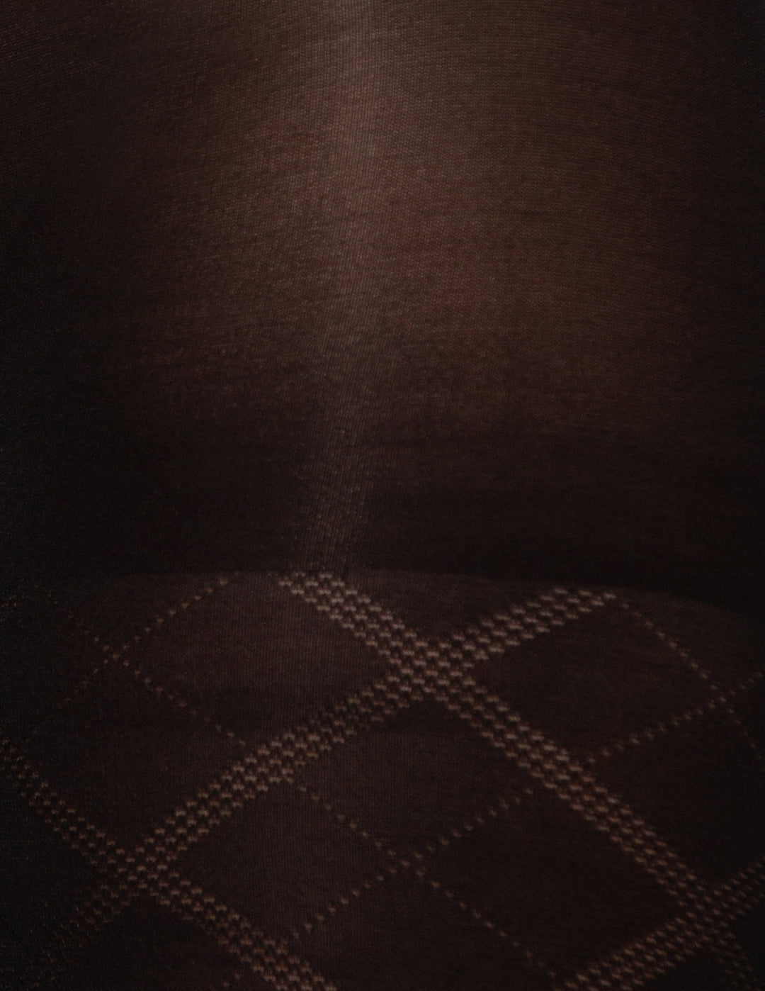 Close-up of a black textured fabric with a subtle diamond plaid pattern visible along the bottom edge.