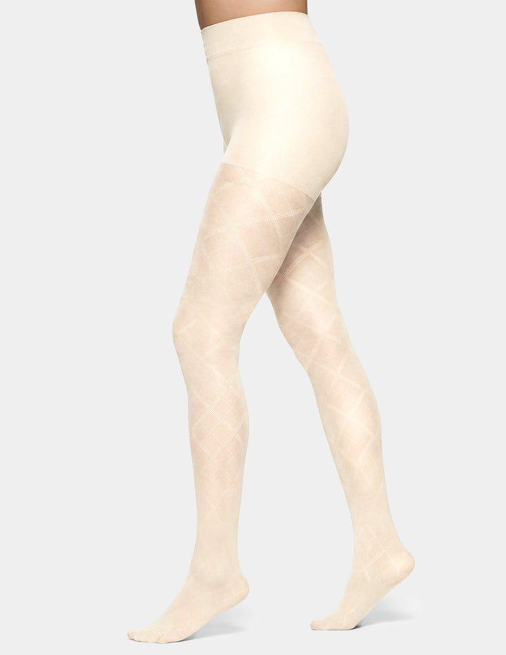 A model's legs wearing a pair of high-waisted, sheer tights with a subtle diamond argyle pattern in a light cream color, shown against a solid light gray background.
