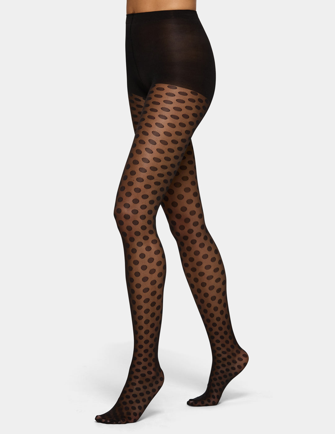 A model's legs wearing sheer black tights with a polka dot pattern, shown against a light gray studio background.