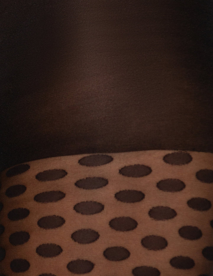 Close-up of a black textured fabric featuring a repeating polka dot pattern.