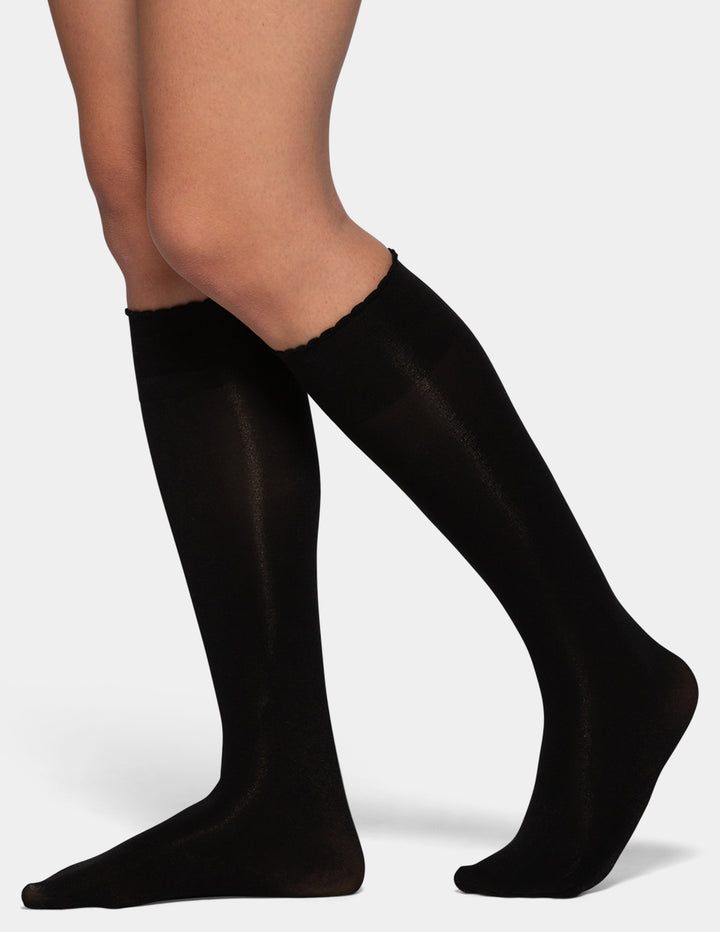 Black knee-high compression socks worn on a model's legs, shown against a light gray background.