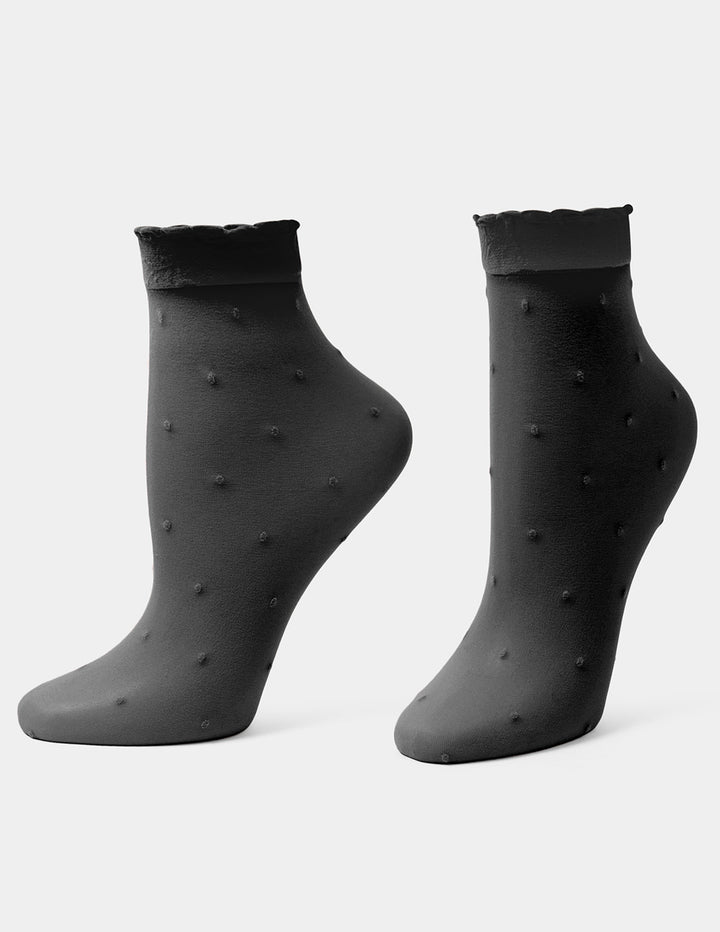 A pair of black ankle socks with a textured, dotted pattern and scalloped cuffs, displayed on foot forms against a light gray background.
