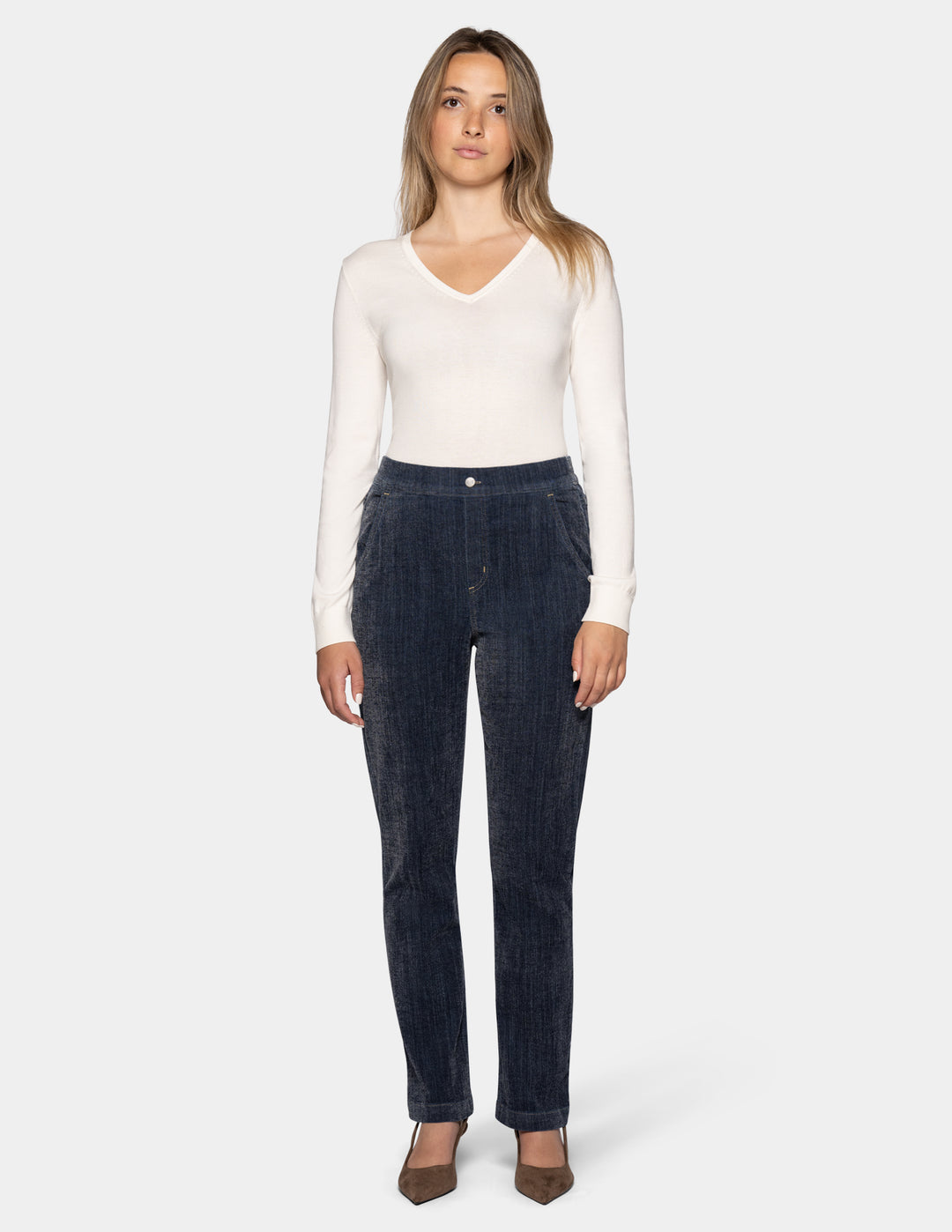 A model wearing dark navy blue denim, a white long-sleeve top, and brown pointed-toe heels against a light gray background.