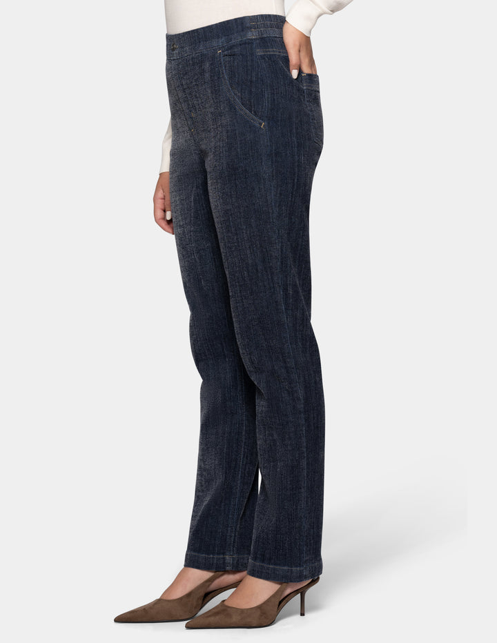 A sideview of a model wearing dark navy blue denim, a white long-sleeve top, and brown pointed-toe heels against a light gray background.