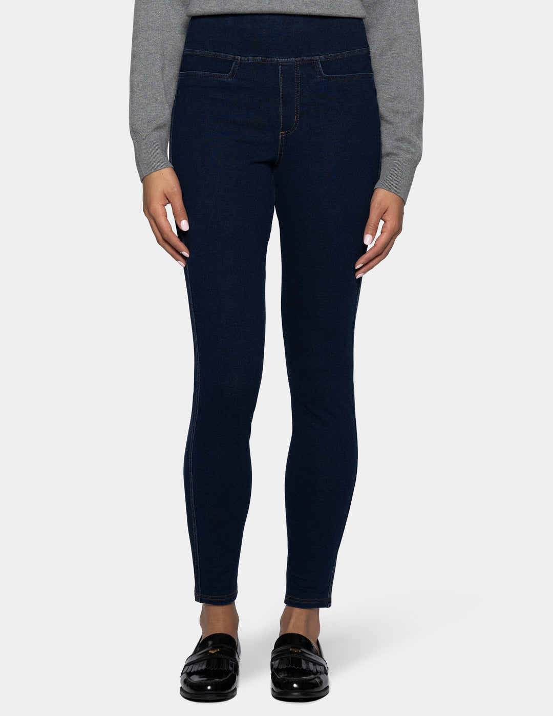 A model from the waist down wearing dark navy blue leggings, a gray long-sleeve top, and black patent leather loafers, set against a plain light gray background.