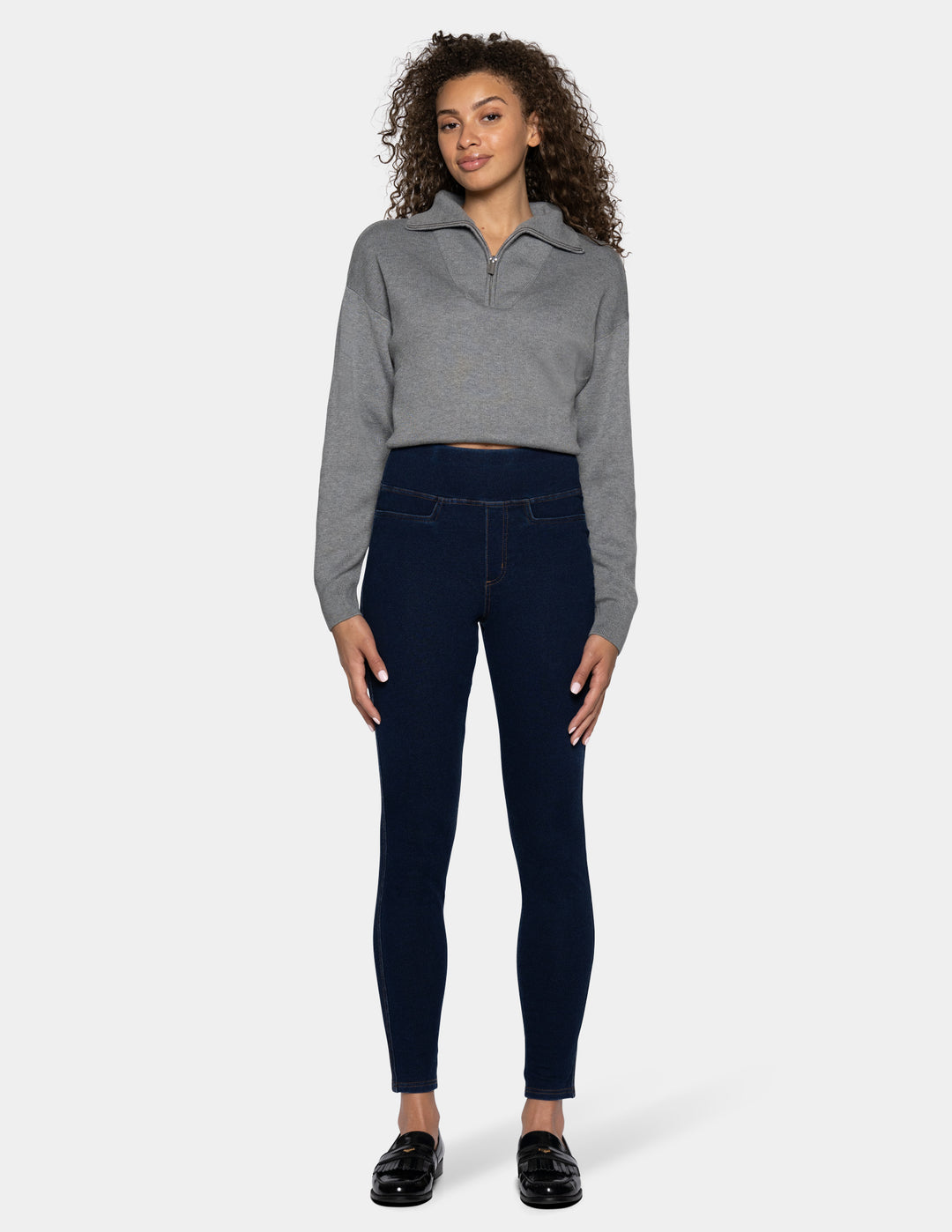 A woman modeling a gray cropped long-sleeve polo shirt and dark navy blue leggings against a light gray background.