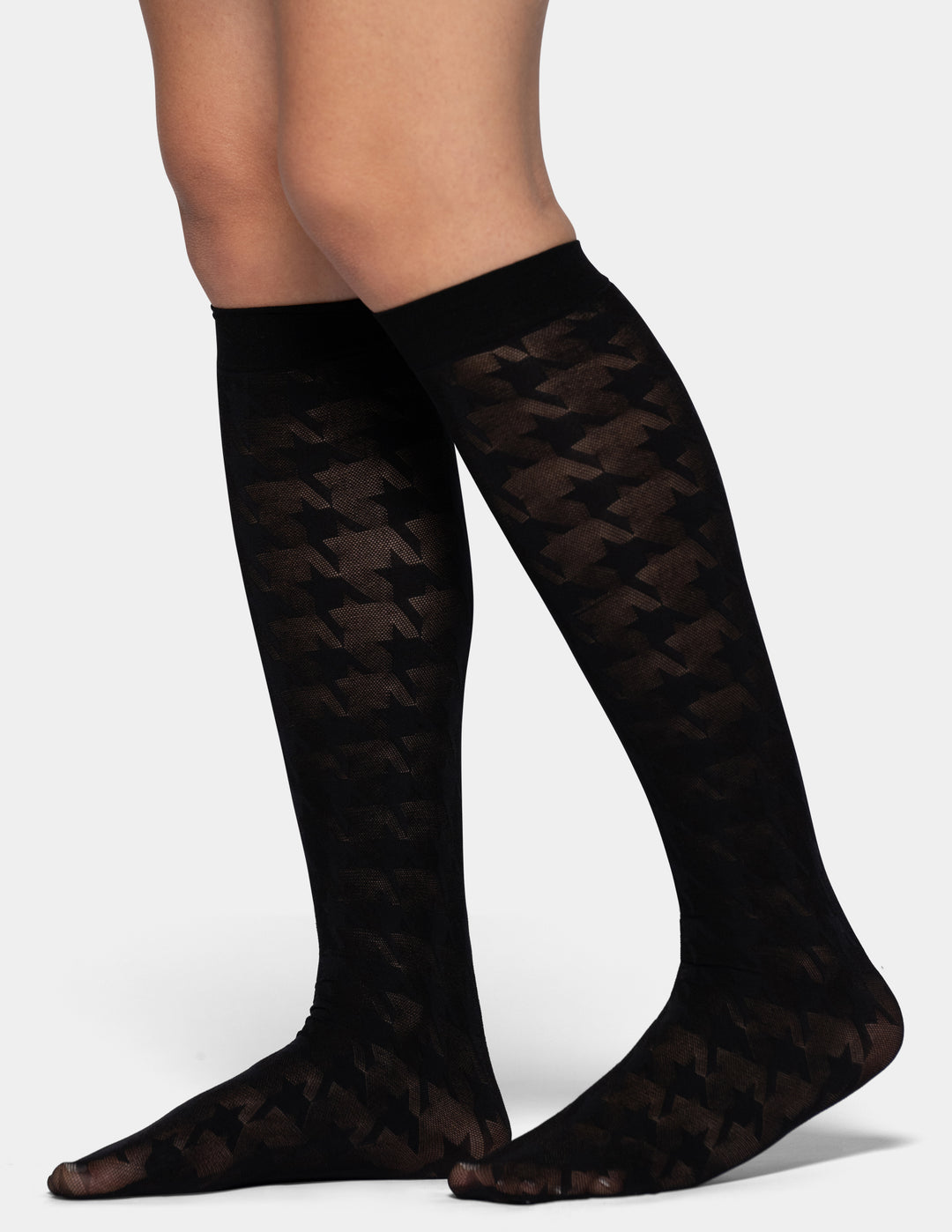 Black knee-high socks with a sheer houndstooth pattern, shown on a model's legs against a light gray background.